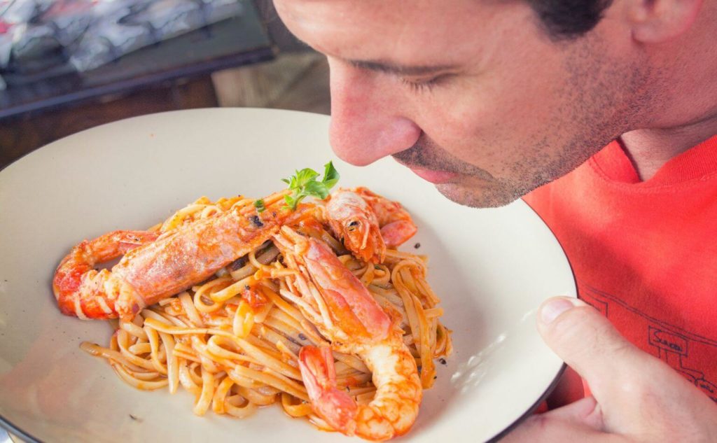 man smelling the aroma of prawn pasta from a restaurant
