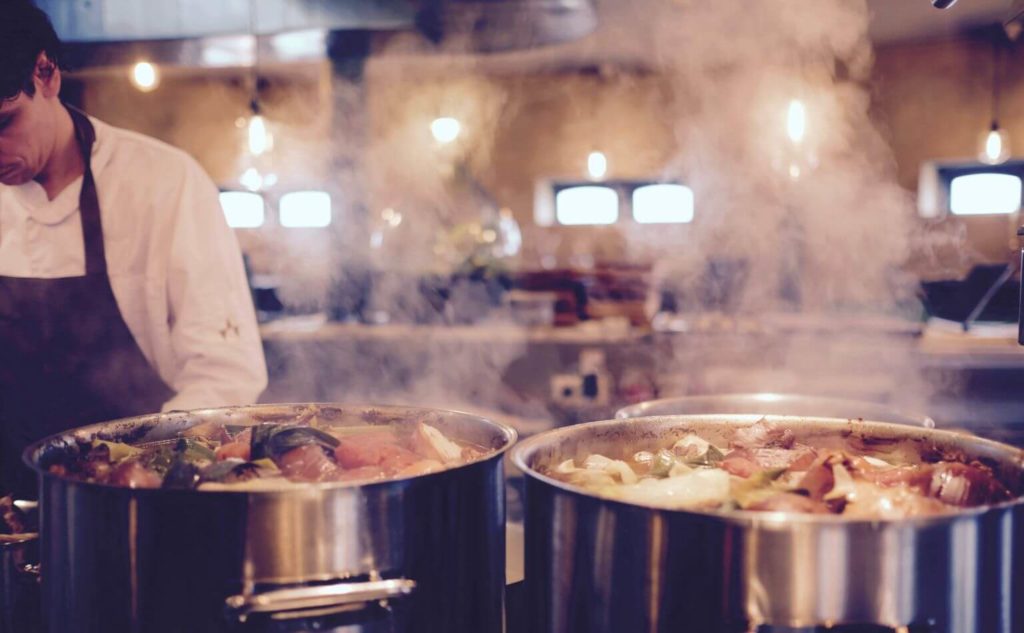 chefs cooking 2 big pots of of delicious smelling food in a restaurant kitchen